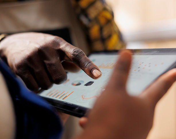 Two people looking at charts on a tablet screen, one of them pointing at a bar chart.