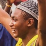 A young man in an embroidered cap smiling at a community event.